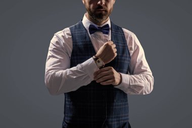 Papyonlu beyefendi lüks bilek saatinde gösteriş yapıyor. Gri renkli papyonlu erkek aksesuar giyiyor..
