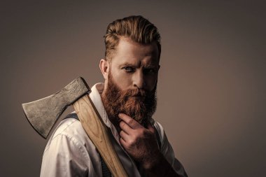 Sakallı adam, baltayı tut. Saç ve sakal bakımı. Yakışıklı, sakallı, vahşi adam. Sakal şekillendirme. Bıyıklı, Kafkas bir hippi. Sakallı adam gri yolda izole edilmiş. Klasik berber dükkanı..