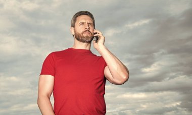 man has phone talk on sky background, conversation. man has phone talk outdoor. man has phone talk wear red tshirt. photo of man has phone talk.