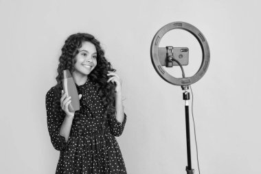 Uzun kıvırcık saçlı mutlu çocuk blog şampuanı için video yapıyor..