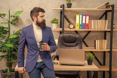 Takım elbiseli, çay ya da kahve içen ciddi bir işadamı ofis masasında oturuyor, mola veriyor..