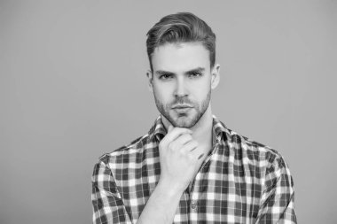 Erkek güzelliği ve saç stili. Gündelik giyinen milenyum adamı. Yakışıklı genç adam. Sıradan gömlekli bir adamın portresi. Gri üzerinde kollarını çapraz tutuyor. Tıraşsız erkek derisi. Sana şehvetli bakışlar atıyor..