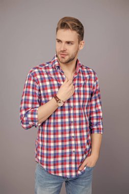 Erkek güzelliği ve saç stili. Gündelik giyinen milenyum adamı. Yakışıklı genç adam. Sıradan gömlekli bir adamın portresi. Gri üzerinde kollarını çapraz tutuyor. Tıraşsız erkek derisi. Genç model..