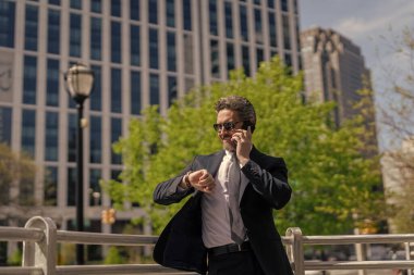 Takım elbiseli bir adam telefonda konuşuyor. Telefonu olan orta yaşlı İspanyol işadamı. İş iletişimi. İş adamının dışarıyı araması gerekiyor. İş adamı telefon kullanıyor ve saati kontrol ediyor.