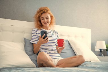 Telefonda internette kahve sörfü yapan mutlu bir kadın. Evde telefonuyla internette sörf yapan bir kadın. Kadının evinde internet sörfü.