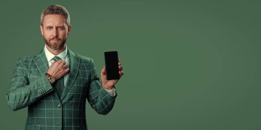 İş uygulamasının reklamı. İspanyol iş adamı telefon ekranını sunuyor. İş adamı yeşilde izole edilmiş bir telefon gösteriyor. Takım elbiseli adam. Yeni telefon uygulaması. Uzay afişini kopyala. Ürünü sunuyorum..