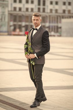 Smokinli zarif bir damat. Damat dışarıda smokin papyon takıyor. Gül ile yakışıklı damat.