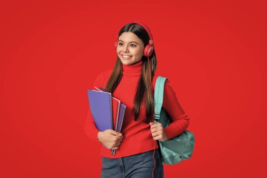 Okul çantalı genç kız kulaklık eğitimi almış. Çalışma kitabı kırmızı üzerine izole edilmiş..