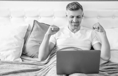 happy mature man working on laptop in bed.