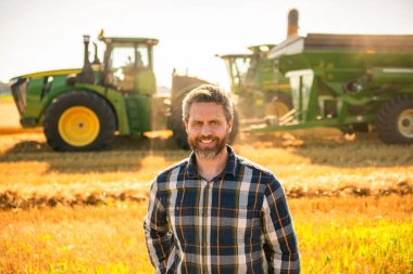 Kareli tişörtlü çiftçi ziraatçi adam hasat makinesiyle hasat hasadıyla tarlada duruyor..