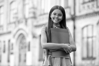 Okula dönelim. Eğitim ve bilgi. Okul çantası takan ve egzersiz kitabı tutan öğrenci kız. İlkokulun dışındaki mutlu genç kızın portresi. Gözlüklü kız öğrenci. Reklam..