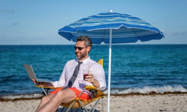 Çevrimiçi serbest çalışma. Dizüstü bilgisayarı olan bir işadamı. Kumsalda dizüstü bilgisayar kullanan bir iş adamı. Seyahat ve iş. Sea Beach 'te serbest çalışan bir adam. İş gezginleri için dinlenme yeri.