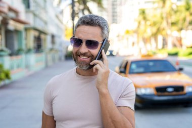 Şehir merkezinde sıradan yakışıklı bir adam telefonda konuşuyor. Şık bir adam dışarıda telefonla konuşurken moda güneş gözlüğü takıyor. Telefonu kullanan olgun bir adam. Şehirdeki erkek telefon konuşmaları. İletişim.