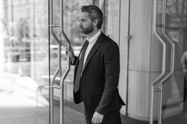 Takım elbiseli Amerikalı işadamı ofis binasını terk ediyor. CEO ofise giriyor. İş adamı. Başarılı bir iş adamı ofise giriyor. Ofis kapısında olgun bir girişimci..