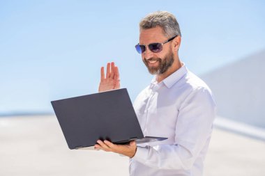 Video konferansı. Dışarıda dizüstü bilgisayarda çalışan bir iş adamı. Adamın iş görüşmeleri var. Başarılı iş adamı çevrimiçi olarak serbest çalışıyor. İnternette çalışan bir iş adamı. Uzaktan kumanda çalışıyor. Çevrimiçi iletişim.