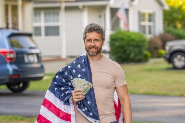 Vatansever adam. Amerikan bayrağı ve dolar parası olan adam. Enflasyon konsepti. Amerikan vergi politikası. İspanyol adam ve Amerikan bayrağı. Amerika 'da vergi ödemek. Katma değer vergisi. Vergi ve gümrük vergisi sistemi.