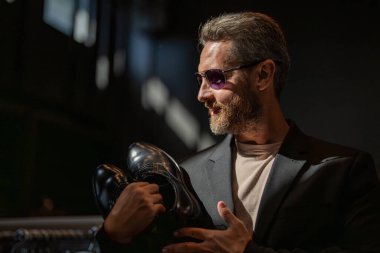 İş adamı dükkanda şık ayakkabılar seçer. Resmi görünmek için klasik deri ayakkabılar. Resmi ayakkabı. Deri ayakkabılar. Ayakkabı mağazasındaki tezgahtar adam klasik ayakkabıları tutuyor. Ayakkabı mağazası afişi.