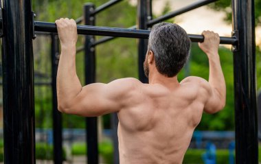 Spor eğitimi. Sporcu adam egzersiz yapıyor. Adam kaslı sırt sporcusu açık hava spor salonunda barfiks çekiyor. Spor yaşam tarzı. Kas kasları ve trisepsler. Güçlü olgun bir sporcu. Adam yanaşıyor..