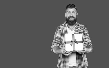 Gri arka planda hediye kutusu olan olgun sakallı adam şaşırdı..