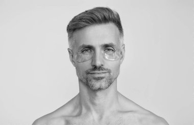 Göz altlarında kolajen pedleri olan bir güzellik uzmanı. Olgun bir adamın gözlerinin altında kolajen bantları olan taze ve sağlıklı bir cildi vardır. Yüz bakımı. Göz bandı takan bir adam. Spa bakımı. Göz bandı. Uzun bir günün ardından uygula.