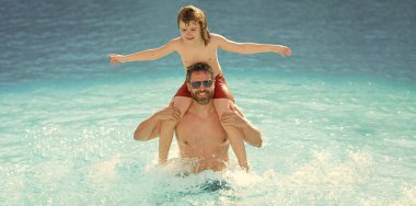 Mutlu bir ailenin yaz tatili. Baba ve oğul yüzme havuzunda. Yazın seyahat. Deniz kıyısı tatili. Oğlu babasıyla eğleniyor. Havuz zamanı. Babalar Günü. Ebeveynlik. Macera seyahati.