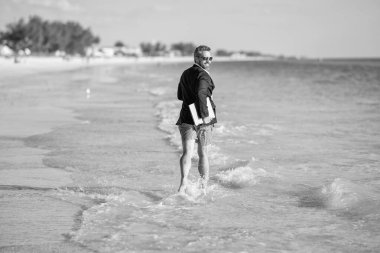 Başarılı bir iş adamı yazın tadını çıkarır. Yaz tatilindeki iş adamı. İnsanoğlunun iş başarısı. Denizde dizüstü bilgisayarla koşan takım elbiseli bir iş adamı. Yaz tatili.