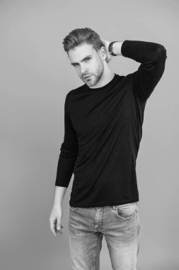 Siyah süveter giyen yakışıklı, genç, beyaz bir adam. Tıraşsız bir yüzü ve gri saç stili var..