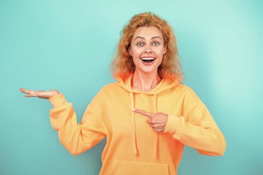 Havalı kapüşonlu giyen kızıl saçlı kız. Maviyle izole edilmiş şık bir kadın. Hareketli moda kız kapüşonlu giyer. Moda kıyafetleri ve tarzı. Kazaklı beyaz bir kadın. Sıradan bir yaşam tarzı. İşaret parmağı.