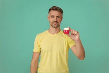 Olgun adam cilt kremi kullanır. Günlük alışkanlık ve kişisel bakım. Cilt güzelliği. Erkek güzellik kozmetiği. Erkek kozmetik ürünü sunan adam. Mavi renkte yüz kremi gösteren bir adam var. Deriyi sulandır..