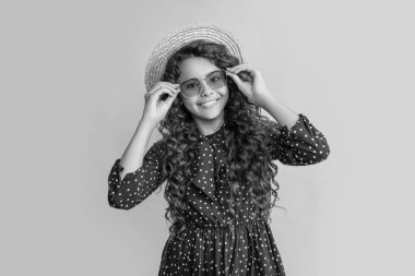 child smile in straw hat and sunglasses with long brunette curly hair on yellow background.