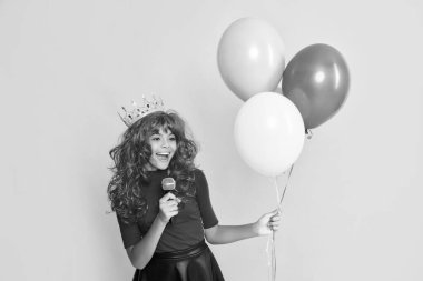 Sarı arka planda mikrofonlu ve parti balonlu mutlu çocuk..