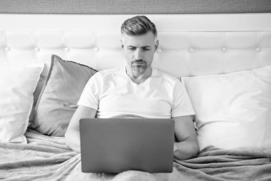 concentrated mature man working on laptop in bed.