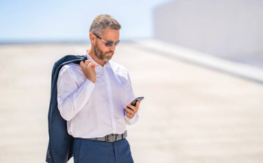 Akıllı telefon kullanan bir iş adamı. İnternette yakışıklı bir iş adamı sohbeti. İş adamı yürüyor. Şirket işi. Dışarıdaki telefonda iş adamı sohbeti. İş adamı yürürken telefonda konuşuyor..