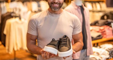 Ayakkabı seçen olgun bir adam. Spor ayakkabıları. Lüks mağazada spor ayakkabıları. Ayakkabı mağazası. Erkek ayakkabısı mağazası. Erkek alışverişi, spor ayakkabılar. Kumaş butikte şık bir adam. Sunulan boyut.