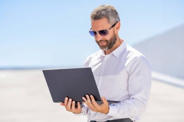 Uzaktan kumanda çalışıyor. Video konferansı. Dışarıda dizüstü bilgisayarda çalışan bir iş adamı. Adamın iş görüşmeleri var. Çevrimiçi pazarlık. Başarılı iş adamı çevrimiçi olarak serbest çalışıyor. Çevrimiçi çalışan iş adamı.