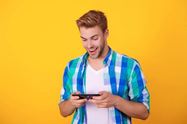Genç milenyum çocuğu çevrimiçi oyun oynuyor. Telefondaki video oyunu. Oyuncu gençliği. Erkek oyuncu akıllı telefonuyla online video oyunu oynuyor. Video oyunu çevrimiçi. Video oyunu ve oyun. Sarı üzerine izole edilmiş adam.
