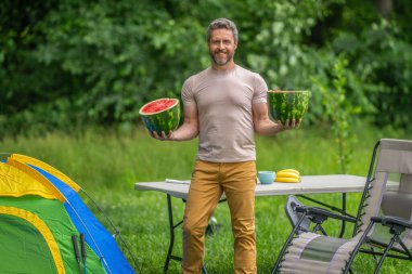 Kampta taze yiyecek. Yaz kampında karpuzlu bir adam. Yaz günü doğa yürüyüşçüsü. Kamp ve doğa pikniği. Adam kampı. Karpuz kampı pikniği. Lezzetli sağlıklı yiyecekler. Doğa geri çekiliyor..