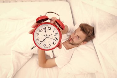 Uyanma ve kalkma vakti geldi. Sabah uyanması. Elinde çalar saatle yatakta yatan uykucu adam. Sabah uyanışı. Uykulu adam çalar saati kapatıyor. Erken kalkmak. Seçici odak ile zaman gösteriliyor.