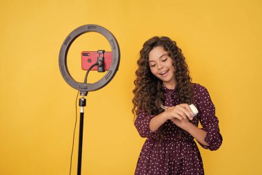 Uzun kıvırcık saçlı mutlu çocuk blogda pudra fırçası için video yapıyor..