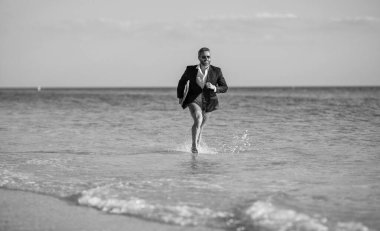 İş adamının iş başarısı. Denizde dizüstü bilgisayarı olan takım elbiseli bir iş adamı. Sahilde dalgıç kıyafetli başarılı bir iş adamı. Yaz tatilinde koşan bir iş adamı. Sahil kenarı aktiviteleri.