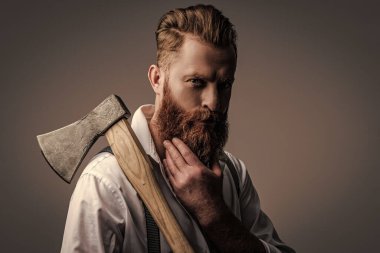 Kızıl sakallı, sakallı, geçmişe dönük pantolon askısı takan vahşi, olgun sakallı bir adam gri baltayı tek başına tutuyor..