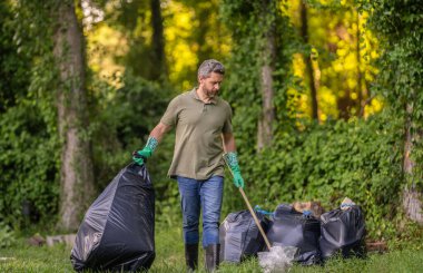 Çevreci adam. Çevresel koruma. Çevreyi koru. Çevre plastik kirliliği. Gönüllü adam ormanda çöp topluyor. Çevresel koruma. Atık azaltma stratejisi.