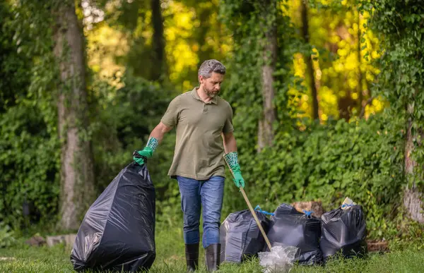 Çevreci adam. Çevresel koruma. Çevreyi koru. Çevre plastik kirliliği. Gönüllü adam ormanda çöp topluyor. Çevresel koruma. Atık azaltma stratejisi.