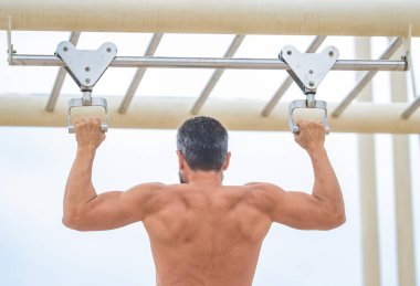 Spor eğitimi. Sporcu adam egzersiz yapıyor. Adam kaslı sırt sporcusu açık hava spor salonunda barfiks çekiyor. Kas kasları ve trisepsler. Güçlü bir atlet. Adam yanaşıyor. Spor barfiks egzersizi.