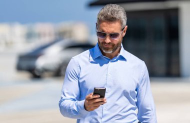 Akıllı telefon kullanan bir iş adamı. İnternette yakışıklı bir iş adamı sohbeti. İş adamı yürüyor. Şirket işi. Dışarıdaki telefonda iş adamı sohbeti. İş adamı telefonda sohbet ediyor. İş anlaşması.