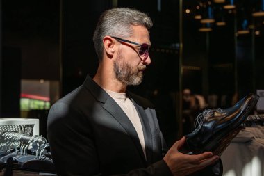Ayakkabı mağazası. İş adamı dükkanda şık ayakkabılar seçer. Resmi görünmek için klasik deri ayakkabılar. Resmi ayakkabı. Deri ayakkabılar. Ayakkabı mağazasındaki tezgahtar adam klasik ayakkabıları tutuyor..