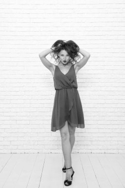 Moda elbisesi içinde genç ve güzel bir kadın. Beyaz tenli kadın, beyazın üzerinde yalnız poz veriyor. Mankenler elbise giyer. Zarif ve zarif bir kadın. Şık, sıradan tarzda şık bir kız. Saçlarına dokunuyor..