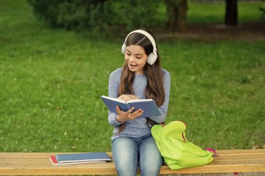 Kızım sesli kitap dinle ve kitap oku. Audiobook kitaba karşı. Öğrenci kız. Okul eğitimi. Liseli kız dışarıda kitap okur ve sesli kitap dinler. Okula dönelim. Eğitim ve bilgi. Merak ediyorum..