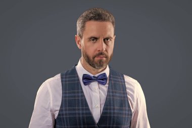 Yakışıklı, karizmatik garson smokin giyer, şık papyon giyer ve gri renkte klasik üniforma giyer..