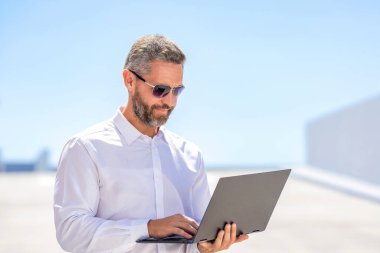 İnternette çalışan bir iş adamı. Uzaktan kumanda çalışıyor. Video konferansı. Dışarıda dizüstü bilgisayarda çalışan bir iş adamı. Adamın iş görüşmeleri var. Başarılı iş adamı çevrimiçi olarak serbest çalışıyor. İnternette toplantı.